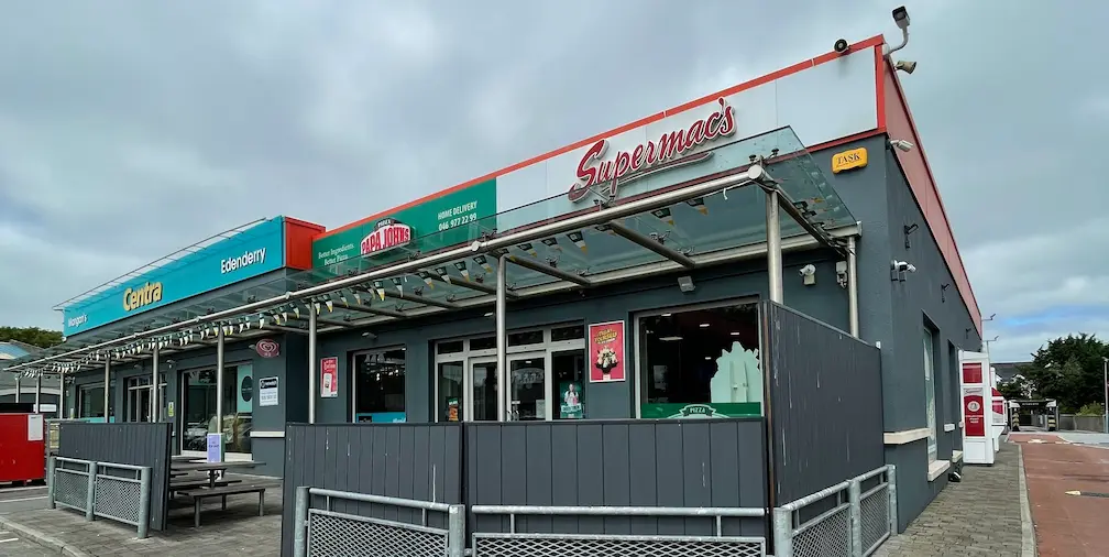Supermac's and Papa John's fast-food restaurant exterior in Edenderry, Ireland. Modern building with shared branding, outdoor seating under a canopy, and adjacent Centra convenience store visible.
