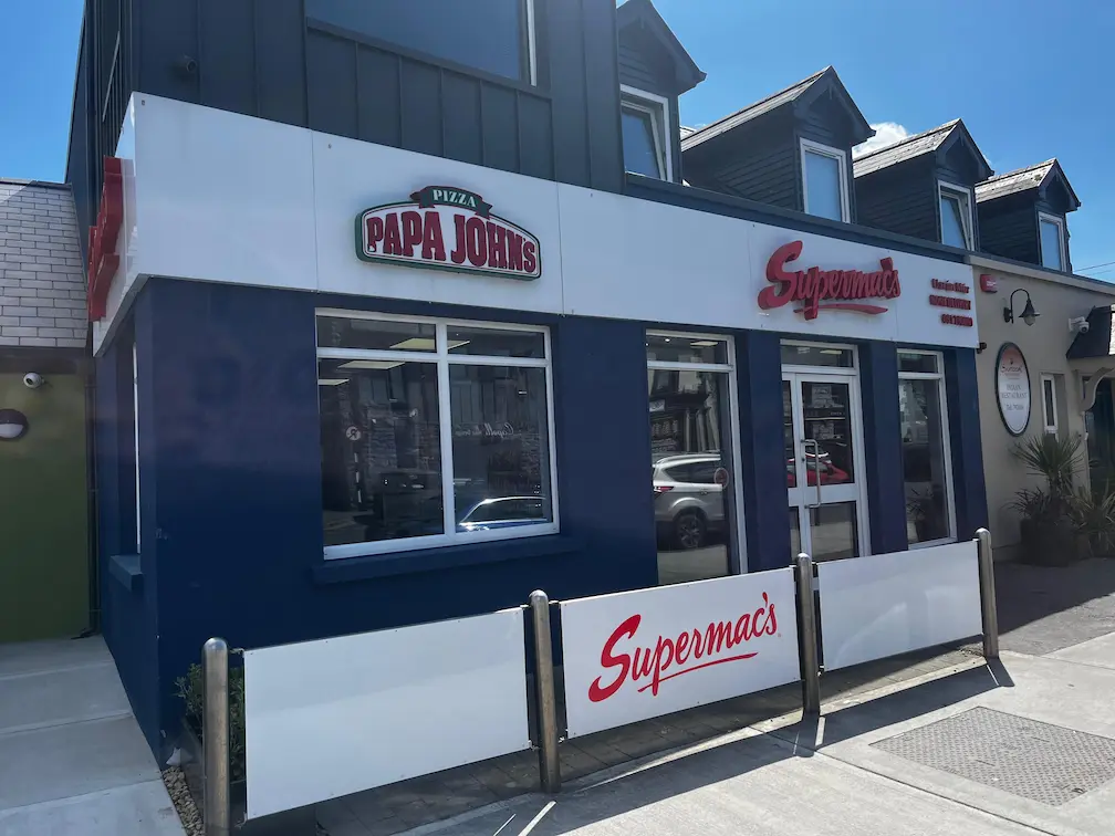 Supermac's and Papa John's restaurant exterior in Oranmore, Ireland. Features a modern blue building with prominent 