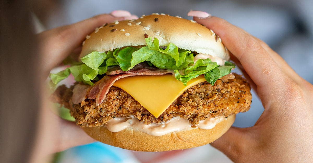 Chicken Breast Sandwich with Bacon and Cheese being handled in preparation of consumption