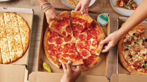 Papa John’s pizzas on a table with hands reaching in to share slices.